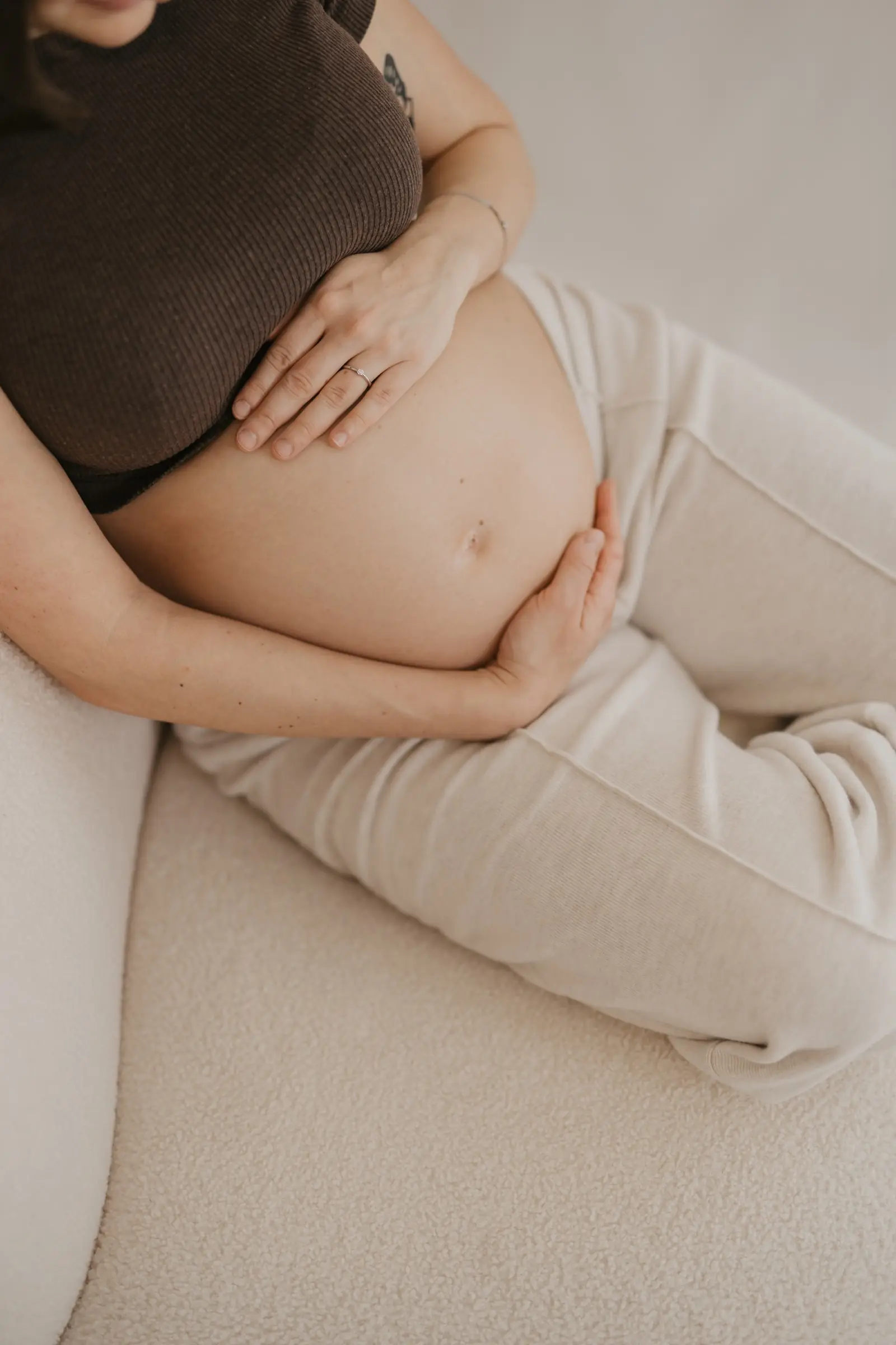 Schwangere sitzt entspannt im Sessel, Hände auf dem Bauch
