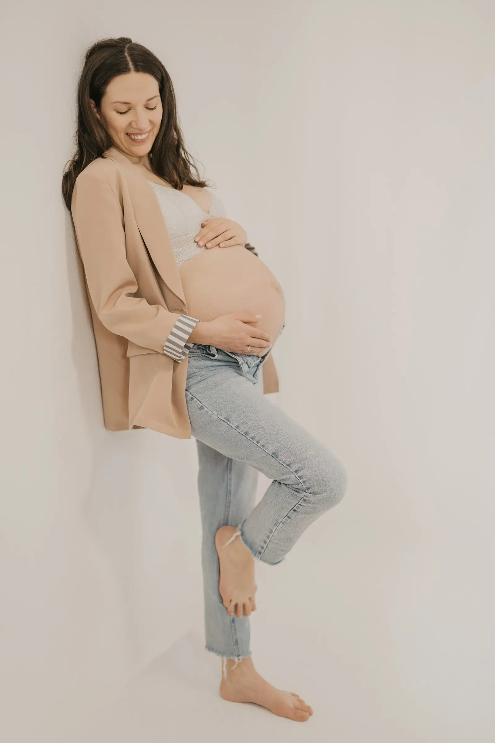 Schwangere lehnt an der Wand und hält den Babybauch