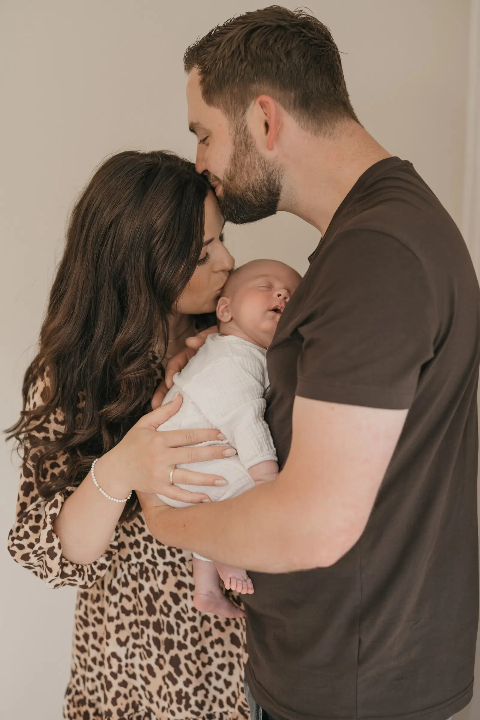 Vater küsst die Mutter auf die Stirn, Baby im Arm