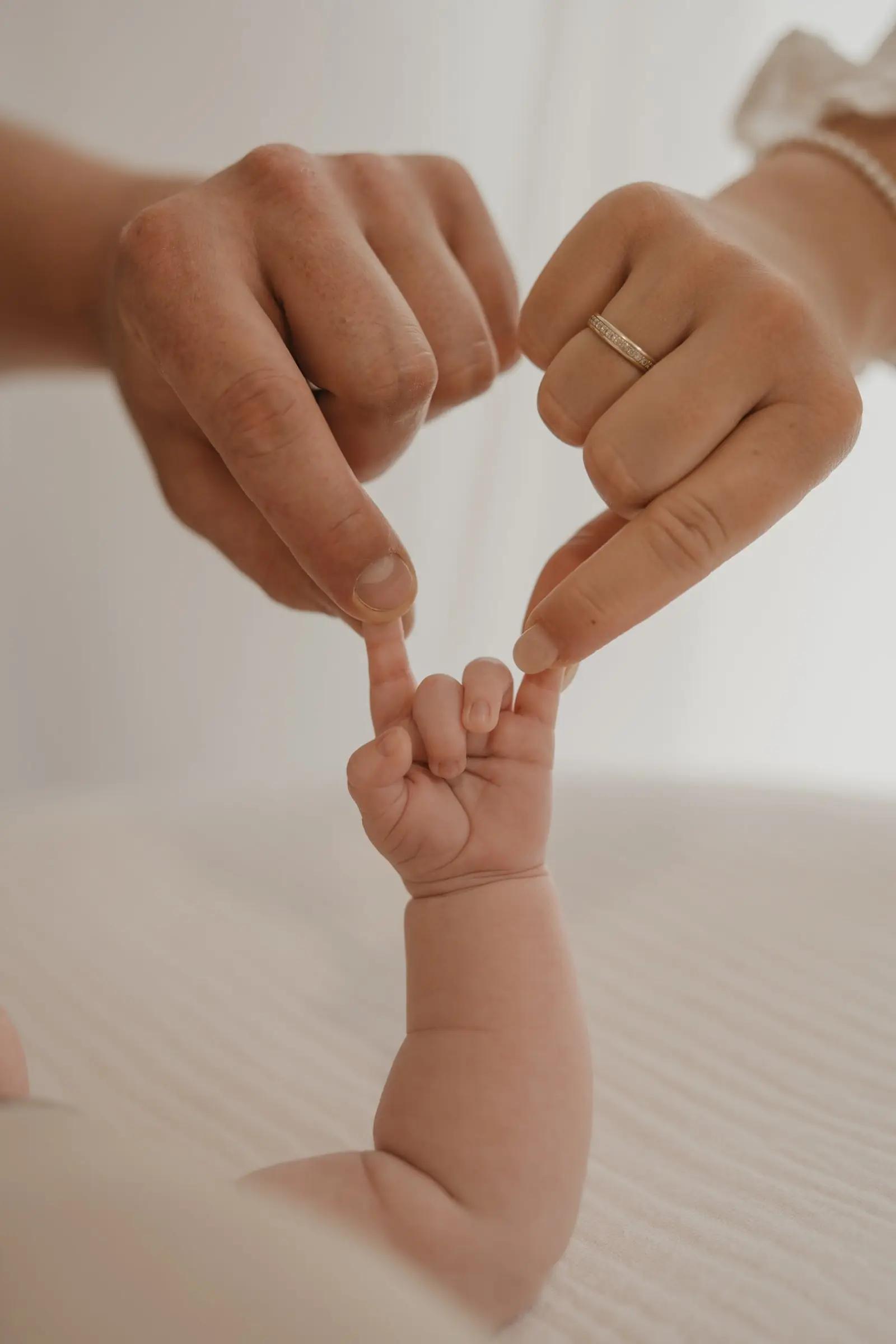 Elternhände formen ein Herz um die Hand des Babys