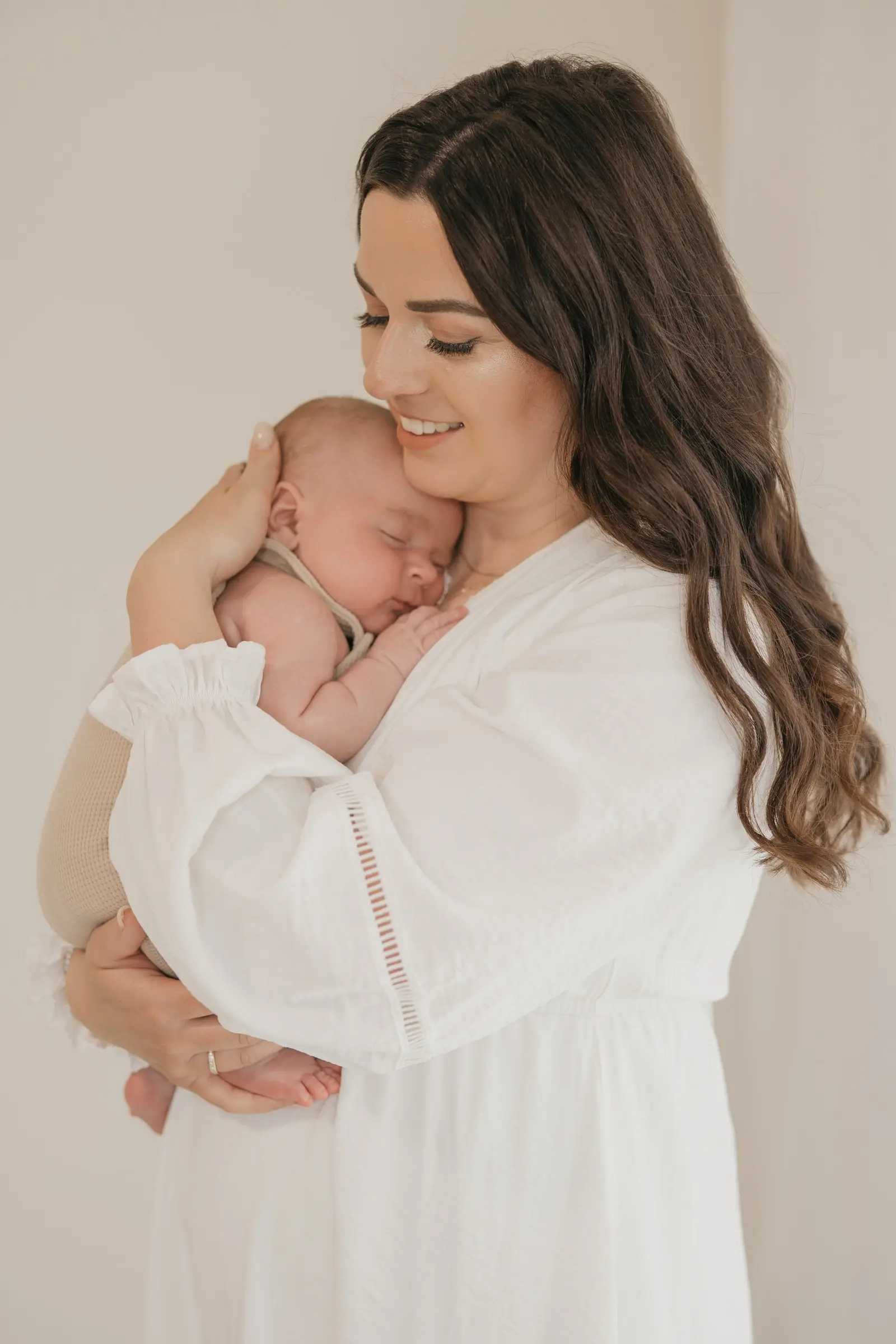 Mutter im weißen Kleid hält ihr schlafendes Baby